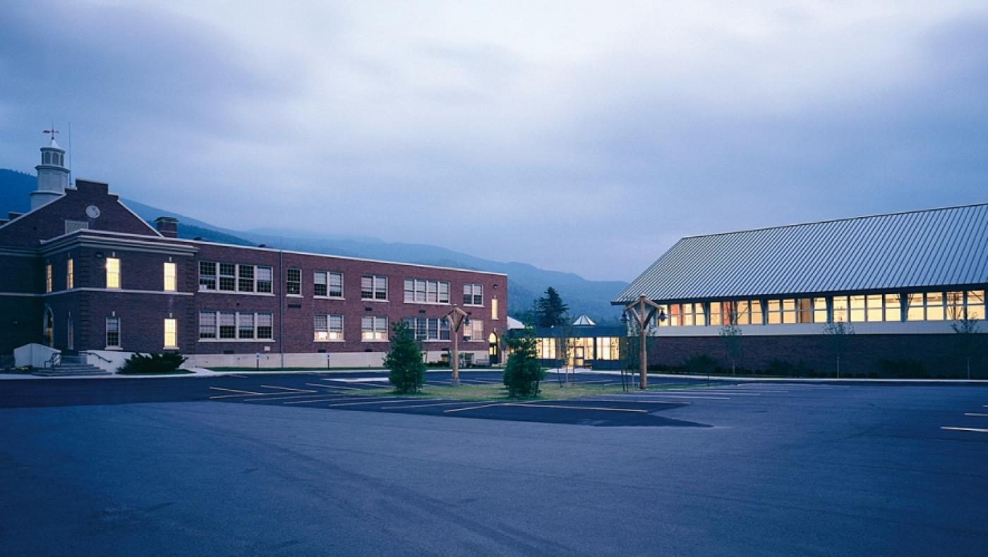 Brick school illuminated from within and surrounded by mountains.