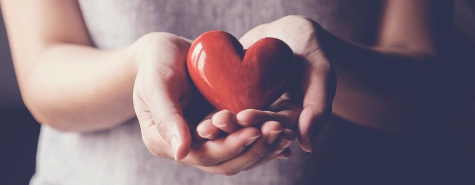Hands holding a red heart shaped polished stone.