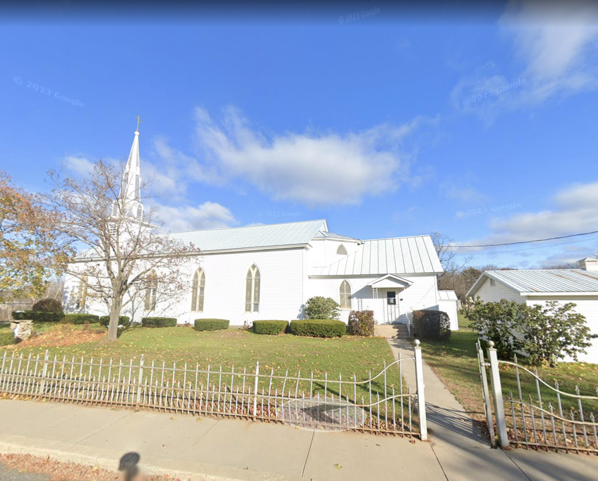 Exterior of the all white Immaculate Conception Church with tall arched windows and white wrought iron fence.