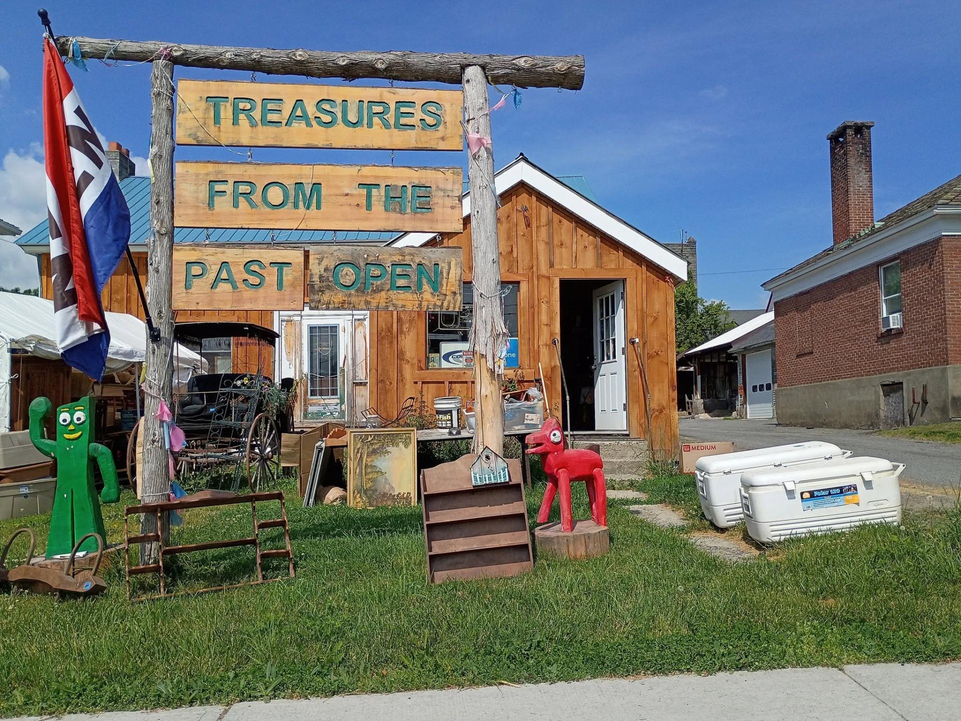 A large raw log sign posts with Treasures From The Past with an open flag flying.