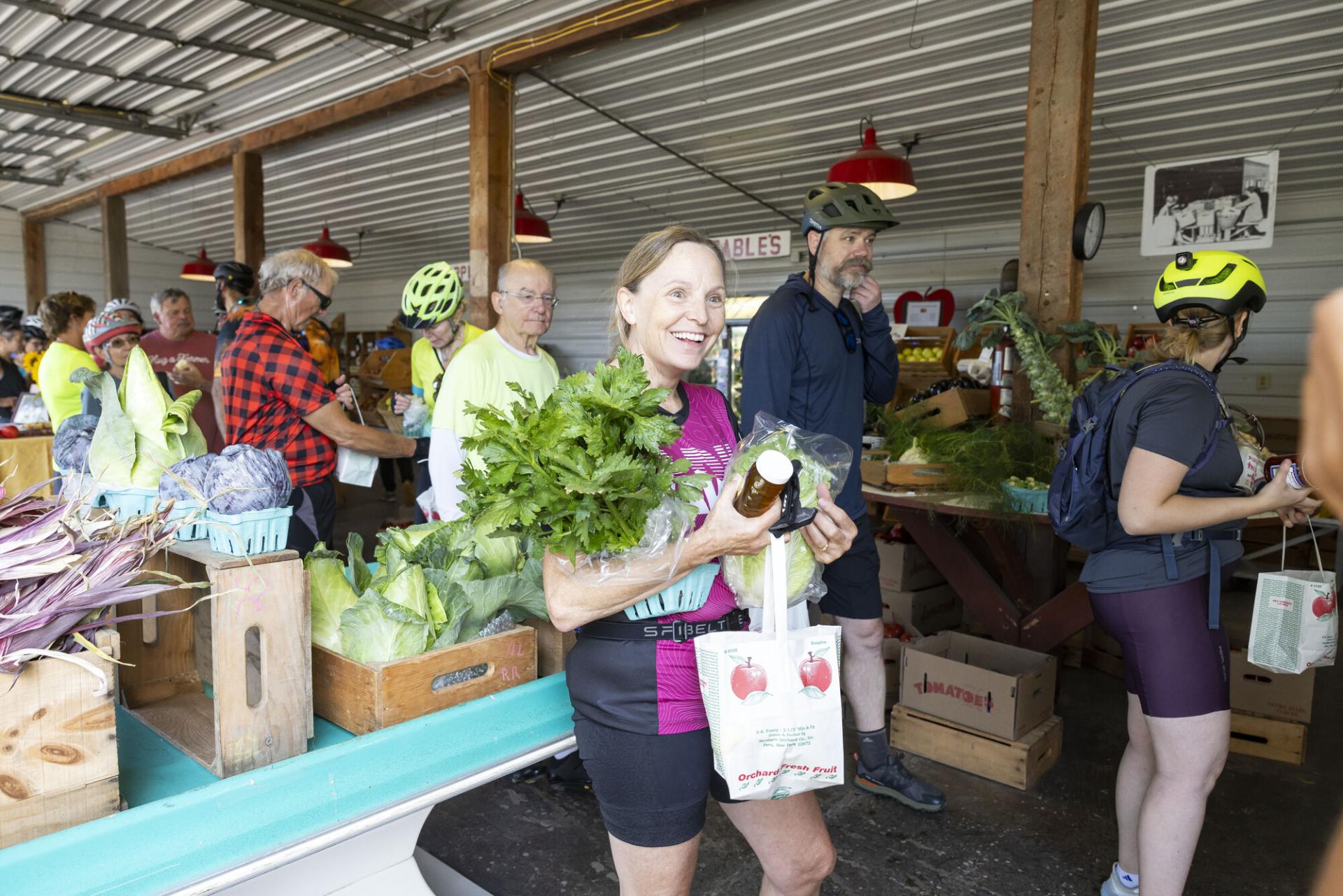 A group of people walk through a farmers market with produce in their hands. 