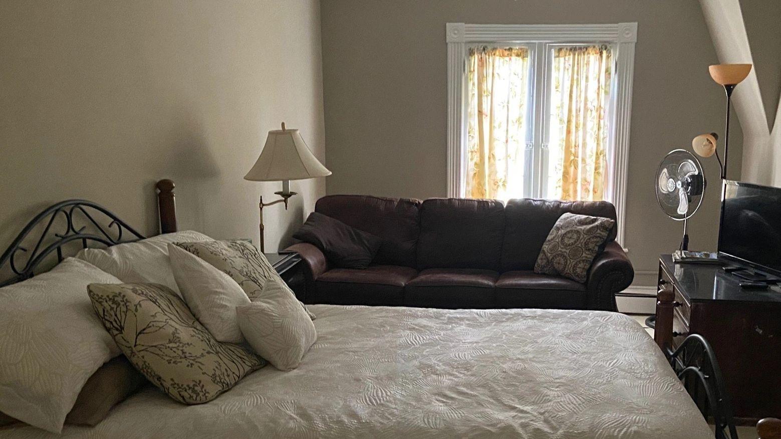 A large bed with bright window and brown couch.
