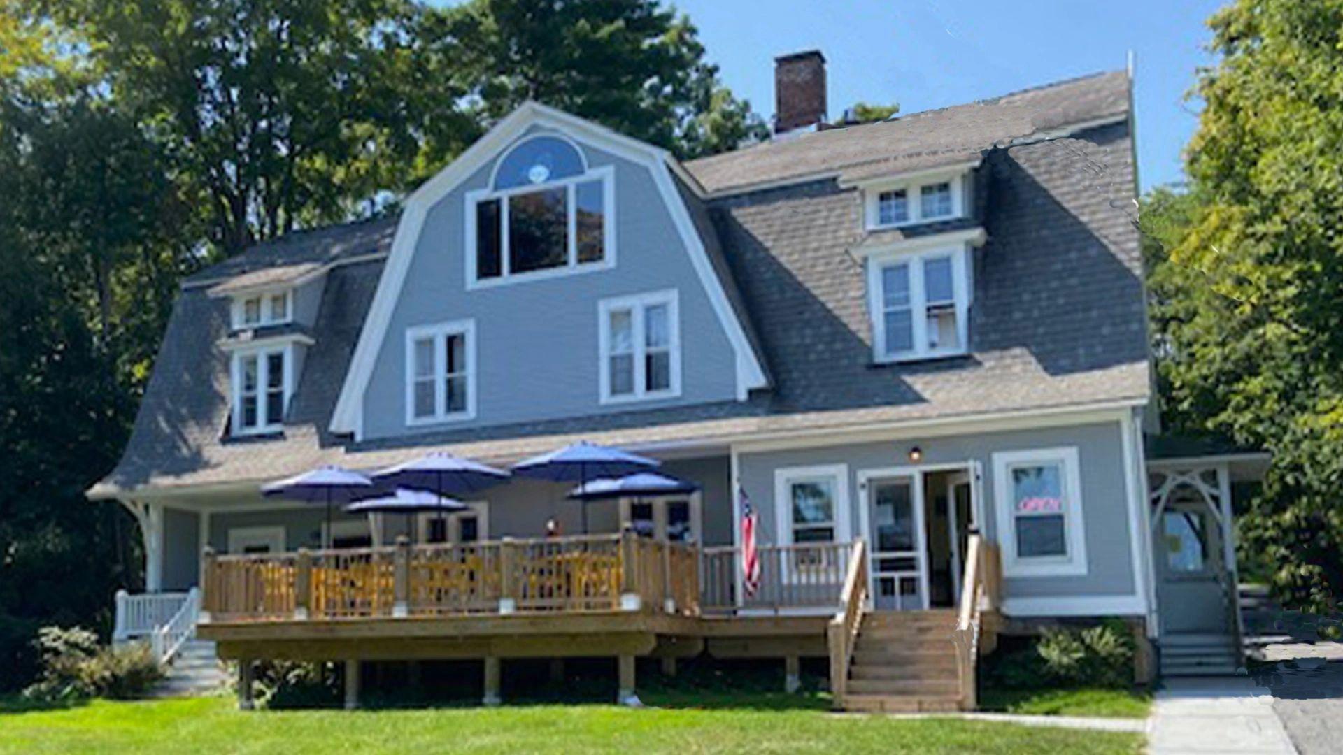 A blue building with white trim and a large deck and front lawn.