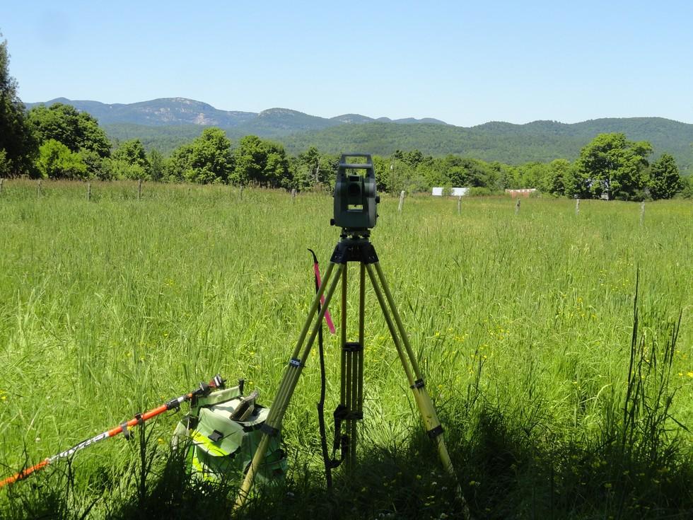 Survey equipment viewing a grassland with mountains in the background.